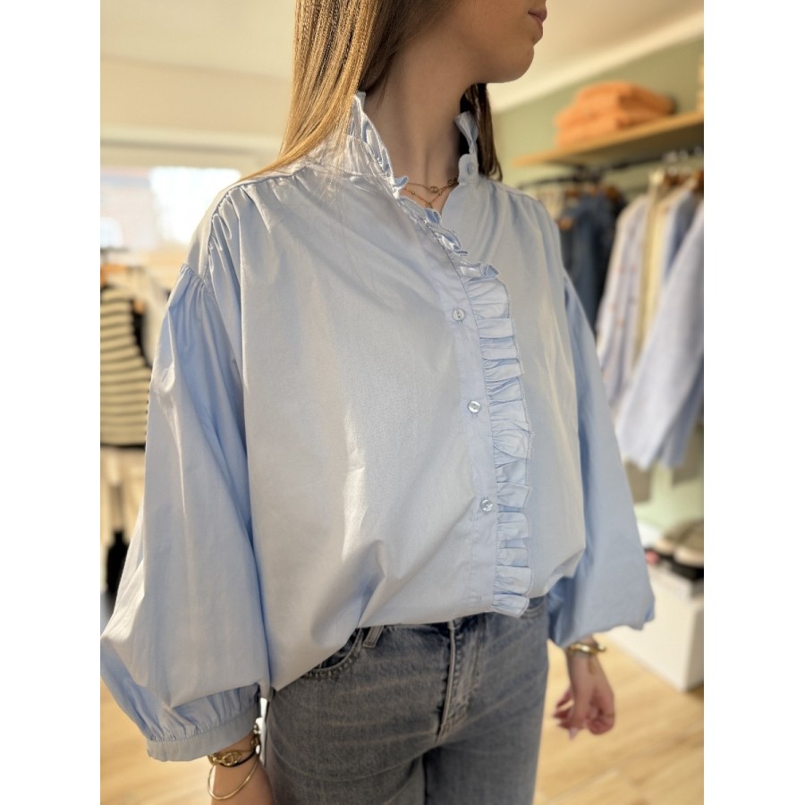 Chemise bleu ciel pour femme avec col montant volanté et détails de volant sur la boutonnière.